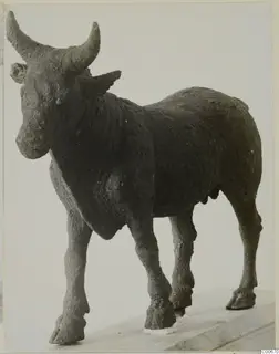 Bronze figure of a bull with long curved horns, standing on a wooden base and seen obliquely from the front.