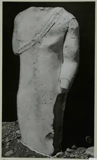 Headless limestone statue torso from Vouni with a band across the chest, standing on gravel.
