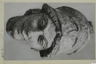 Limestone head from Vouni with a raised helmet-like ridge over the crown, shown on a grey backdrop