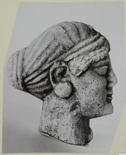Limestone head in right-facing profile, hair drawn back in ridged bands into a bun, with a large disc earring, from Vouni