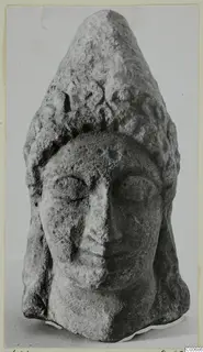 Limestone head with a tall conical headdress, from Vouni, shown frontally against a plain grey background