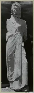 Standing limestone statue of a woman from Vouni, shown against a dark backdrop