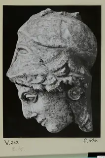 Sculpted limestone head in profile, wearing a helmet, shown against a black background
