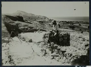 Alfred Westholm seated on a stone wall at the theatre's east entrance at Soli, with a tripod and the sea beyond.