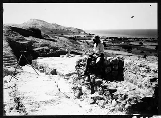 Alfred Westholm seated on a stone wall of the theatre at Soli, with hills, fields and the sea behind.