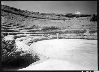 Tiered stone seating of the theatre at Soli, with a single standing figure on the open orchestra floor