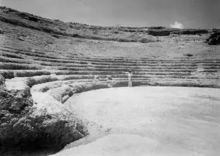 Alfred Westholm standing in the orchestra of the theatre at Soli, with the curved tiers of the cavea rising behind him