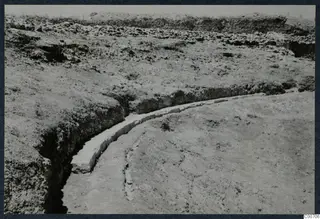 Curved row of pale cut stone blocks running through an excavation trench at Soli, the theatre.