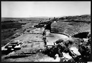 Excavated theatre at Soli, with curved rows of stone seating around a flat area and the sea beyond the plain.