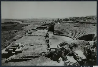 Excavated theatre at Soli with curved stone seating rows, a paved area, and the sea and plain beyond