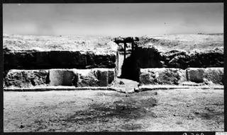 Excavated stone wall with a narrow doorway and a timber crossbeam at Soli theatre