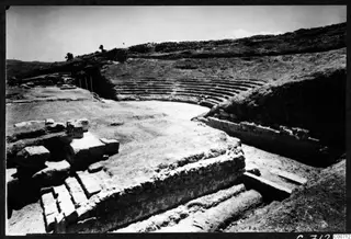 Theatre at Soli: curved stone tiers rise up a hillside around an open level area, with cut stone blocks in the foreground.