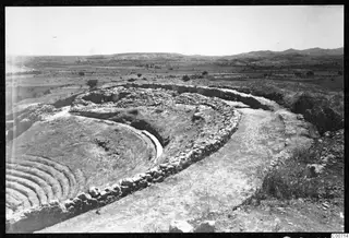The theatre at Soli, with curved stone seating and walls around a cleared area, overlooking a flat plain and hills
