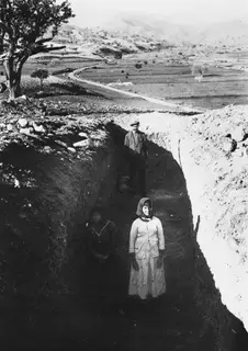 Test trench 2 at Pezoullia, Soli, with a woman standing in the trench and a man behind her, fields and hills beyond