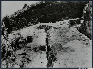 Excavation at the theatre at Soli, showing a narrow cut, stone blocks and a steep bank of earth and rubble.