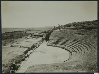 Theatre ruins at Soli with curved rows of stone seating, looking across the flat ground toward the sea and plain.