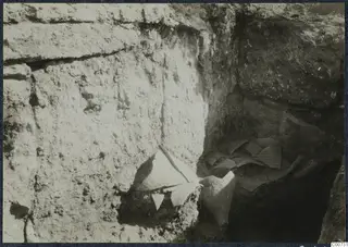 Pottery fragments lying in situ in an excavated trench at Vouni Palace, against a stone wall.