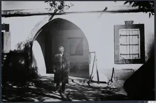 Man in a long coat standing outside the mukhtar's house in Milia, in front of a whitewashed arched doorway