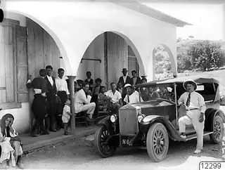 Group of people outside the café in Pyrgos, with an open touring car parked in front of a whitewashed arched building