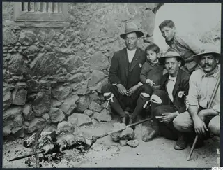 Five people sit by a stone wall beside a whole animal roasting on a spit over a fire at Galini.