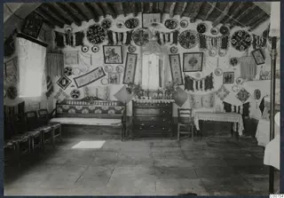 Interior of the mukhtar's best room at Milia, walls hung with embroidered textiles, framed pictures and decorated plates.