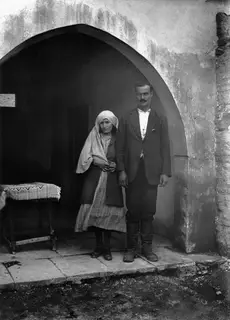 A man and a woman standing together in front of an arched doorway with a plastered wall at Ayios Iakovos.