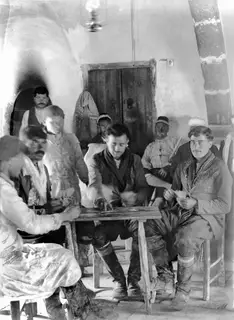 Nine men gathered around a wooden table playing cards in a whitewashed vaulted room at Ayios Iakovos.