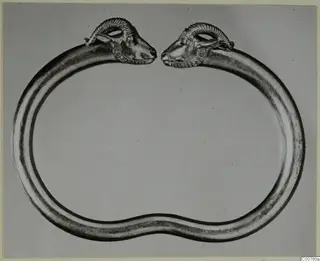 Gold bracelet with two animal heads with curled horns, facing each other across a gap