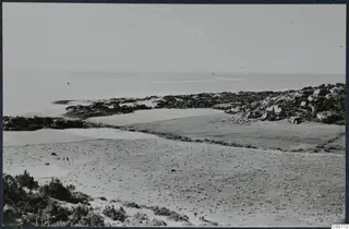 Landscape at Oura with open fields, coastal scrub and rocky outcrops, and the sea beyond