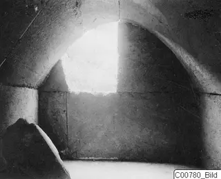 Interior of Trachonas T.1, showing a curved stone ceiling and a bright opening in the back wall