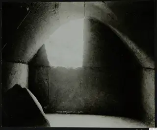 Interior of tomb T.1 at Trachonas, showing an arched stone chamber lit through an opening in the back wall.