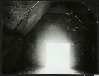 Interior of a stone-built room at Kountoura Trachonia, with sloping stone slabs overhead and a bright opening at the far end.