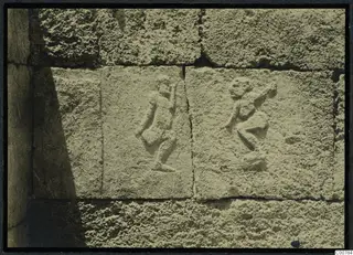 Two small human figures carved in relief on square blocks of a stone wall, Tomb 1 at Trachonas