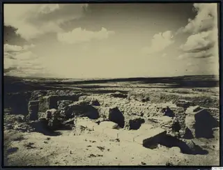 Excavated stone walls and blocks at the Idalion acropolis, with a wide plain and low hills beyond.