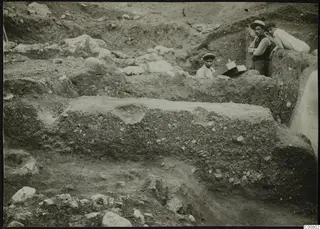 Cross-section of the Plakes E.C. house excavation at Lapithos, with three people at the trench edge.