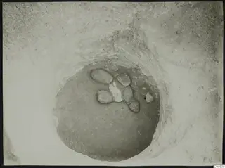 Excavation at Plakes, Lapithos: stones lying in a round pit seen from above, with a pale patch among them.