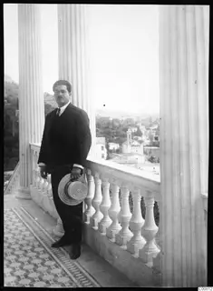Perikles Kaplanis, mayor of Lapithos, standing on a columned balcony holding a straw hat