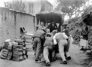 People loading stacked cardboard boxes into a covered cart on a dirt road at Lapithos.