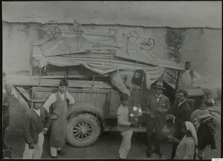 Men and a woman gathered around a loaded lorry at Lapithos, with wooden wheeled frames roped down under canvas on top