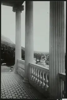 Terrace with fluted columns and a balustrade, overlooking a town and wooded hillside below