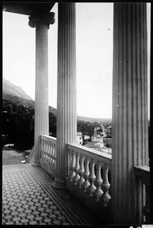 Terrace with fluted columns, a balustrade and a patterned tiled floor, looking over a town with a church tower.