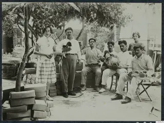Rosa Lindros and Ttoulis Souidos with workmen in a garden in Nicosia, seated and standing under a tree