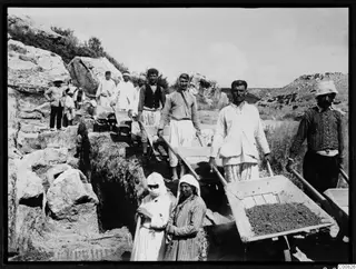 Workers with wheelbarrows and tools in an excavation trench at Oura