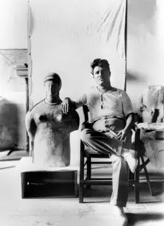 Toulis Souidos seated in a wooden chair, his arm resting on a large sculpted head and torso