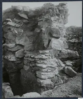 Standing wall of rough stone blocks at the Idalion acropolis excavation, with fallen stones and soil at its base.
