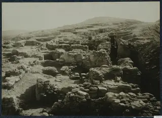 Excavated stone walls and foundations on the Idalion acropolis, with a deep cutting on the right and a hill behind.