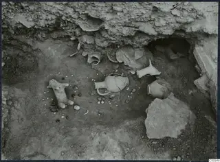 Excavated pit at Idalion Acropolis with pottery vessels, a small animal-shaped vessel and scattered stones on the floor