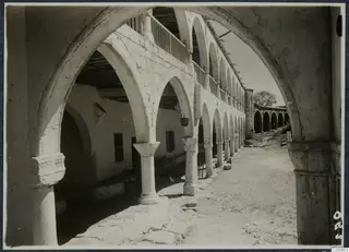 Monastery courtyard at Lambousa, seen along a stone arcade of pointed arches with a balcony on the upper storey