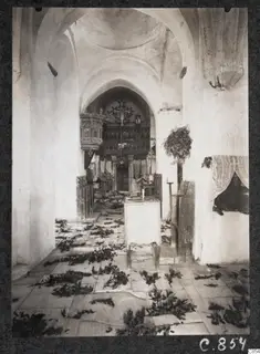 Interior of the monastery church at Lambousa, its floor strewn with leafy branches, with a carved wooden screen and cross beyond