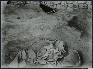 Excavation at Idalion Acropolis with broken pottery sherds lying in the soil beside a stone wall.